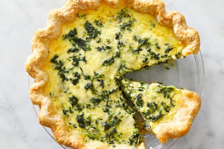 A spinach quiche in a glass pie dish with one slice taken out and another separated from the rest of the quiche.