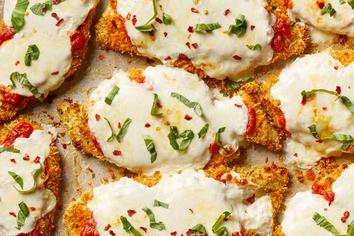 Overhead shot of baked chicken parmesan on a sheet pan, topped with red pepper flakes and basil.