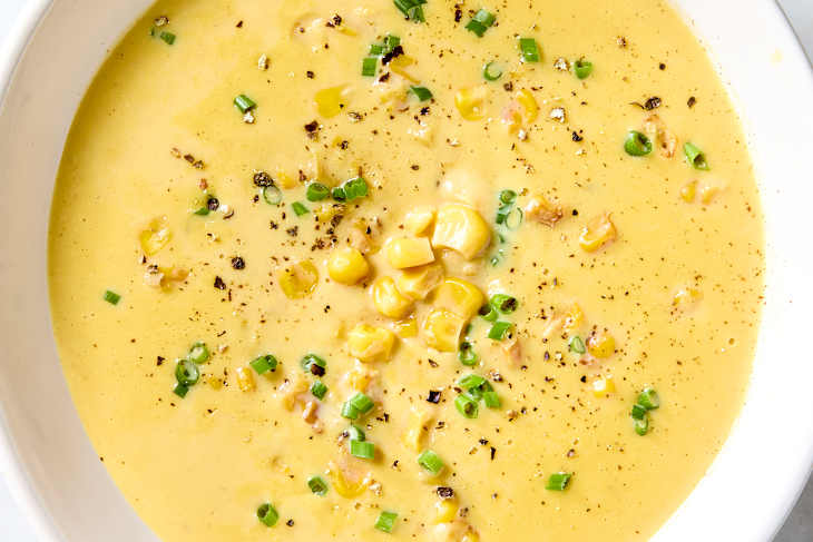 Overhead shot of corn soup in a white bowl, topped with green onion and black pepper.