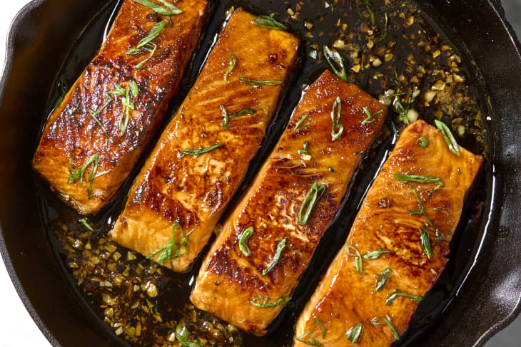 Overhead shot of four cooked pieces of salmon in a cast iron, topped with green onion.