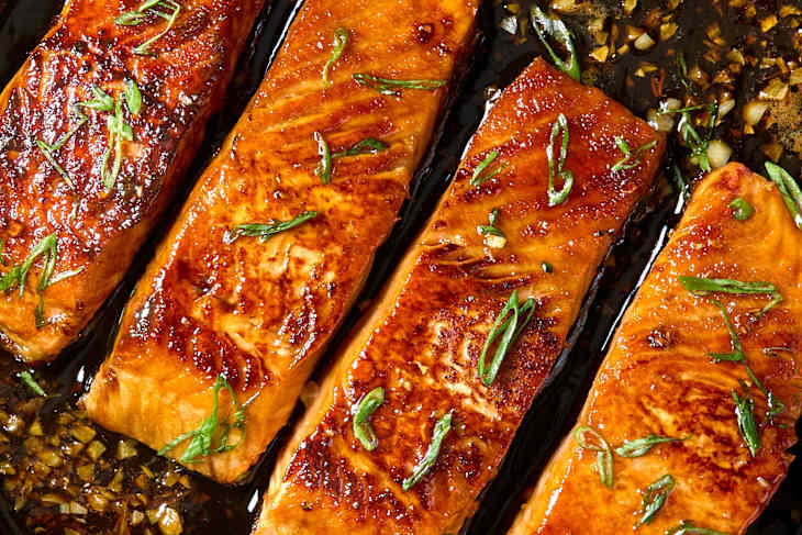 Overhead shot of four cooked pieces of salmon in a cast iron, topped with green onion.