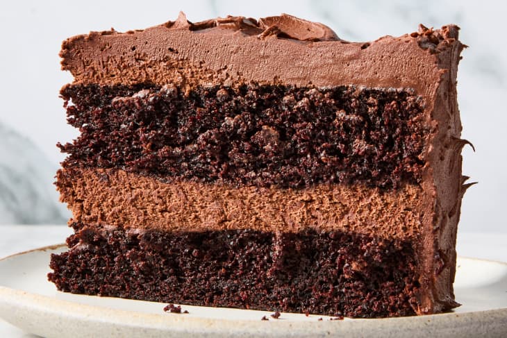 head on shot of a piece of chocolate cake with chocolate icing, on a white plate.