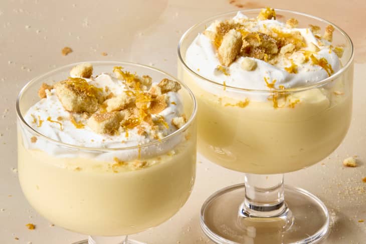 angled shot of a two dessert glasses with orange creamsicle mousse, topped with whipped cream, crushed nilla wafers and orange shavings.