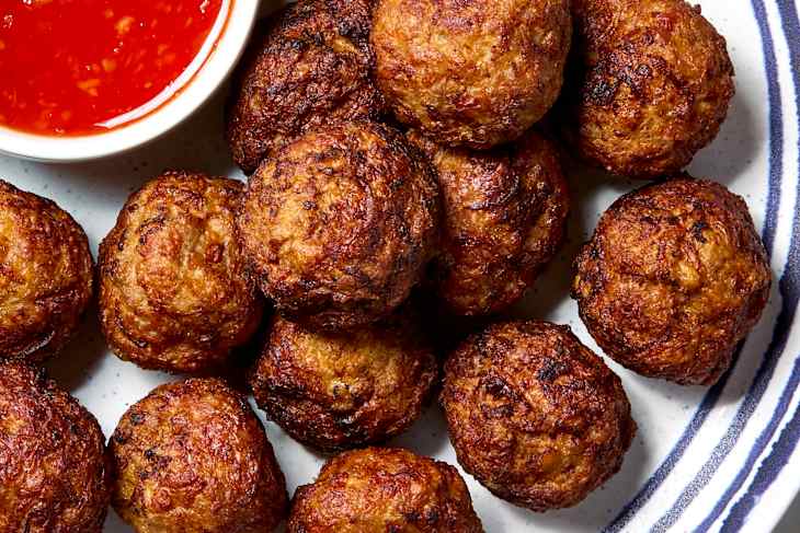 overhead shot of meatballs piled on a plate with a small bowl of sweet chili sauce.