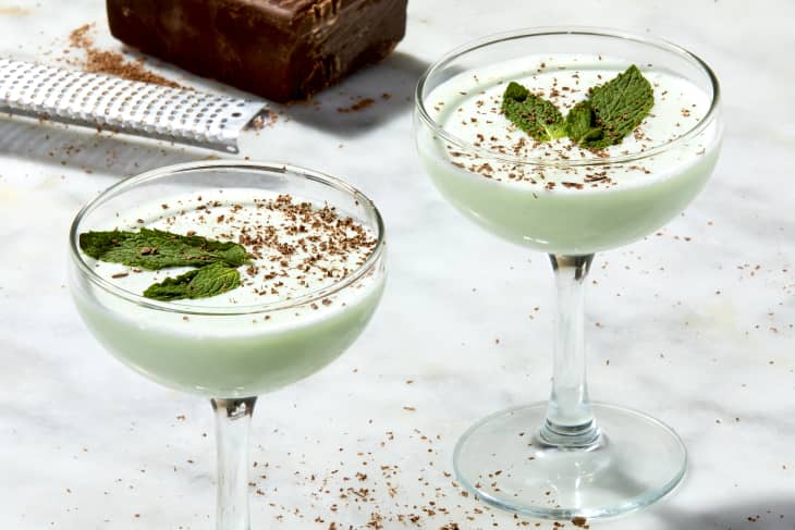 angled shot of two grasshopper cocktails on a marble surface, garnished with chocolate shavings and mint.
