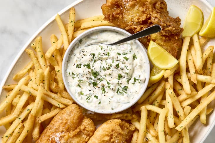 overhead shot of fish and chips on a platter, with a bowl of tartar sauce in the middle of the platter - topped with herbs.