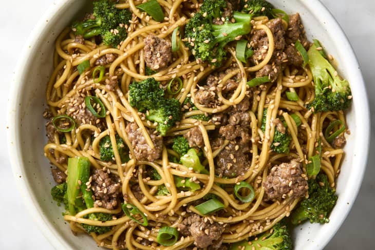 overhead shot of beef and broccoli noodles in a small white bowl, topped with sesame seeds