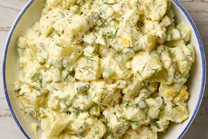 overhead shot of potato salad in a white bowl with a blue rim, topped with dill