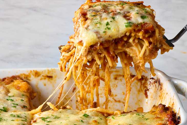 head on shot of baked spaghetti in a baking dish, with a piece taken out of the dish