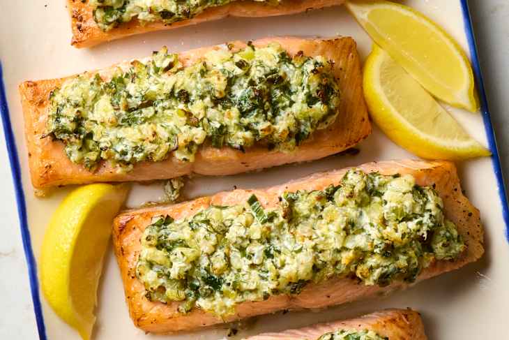 overhead shot of three pieces of salmon rockefeller on a plate with lemon wedges