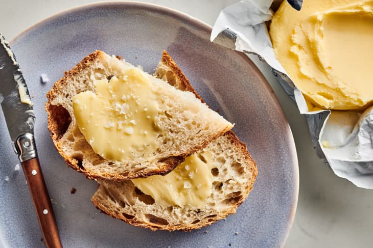 cultured butter is spread on top of toast that sits on a plate with knife and butter package next to it