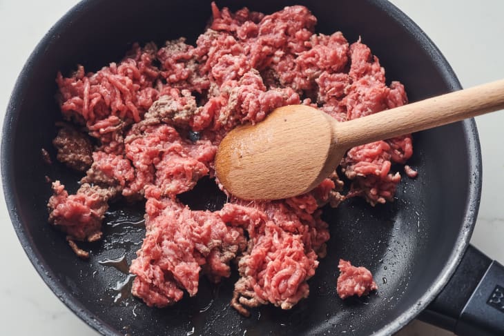 someone is stirring ground beef with a wooden spoon