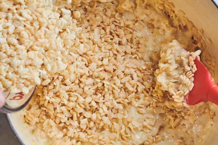 someone is pouring rice krispies into pot with marshmallow and other rice krispies