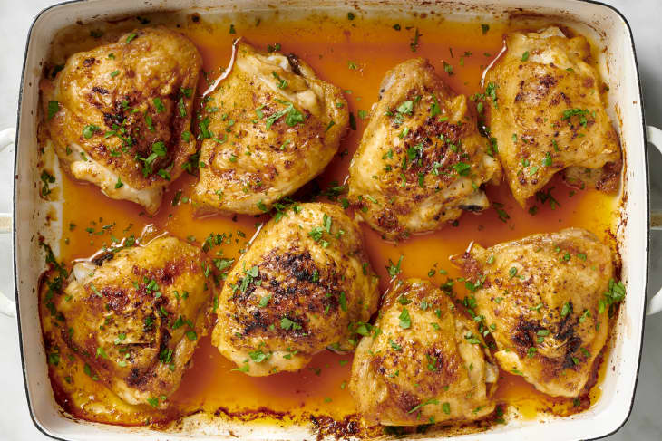 Overhead view of cooked chicken thighs in a white pan topped with herbs.