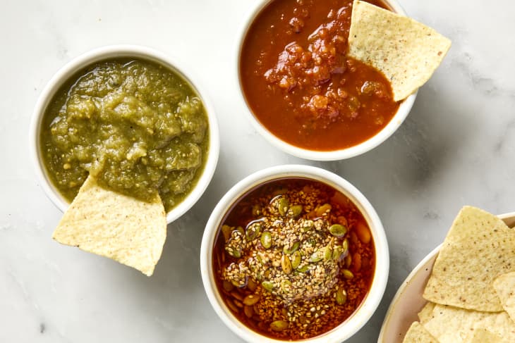 overhead shot of three different salsas: tomatillo, chipotle and salsa macha, in small bowls, with chips being dipped