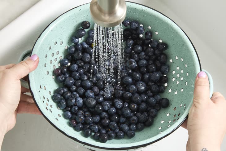 overhead shot of berries getting rinsed in a light blue colander in the sink