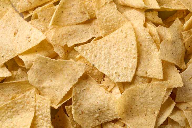 Xochitl brand white corn tortilla chips scattered on a marble surface.