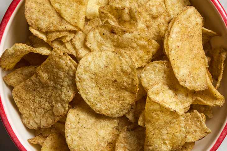Bowl filled with golden-brown potato chips, lightly seasoned and stacked.