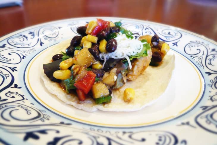 Taco topped with black beans, corn, diced tomatoes, and shredded cheese on a decorative plate.