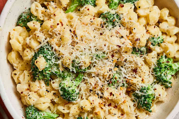 Creamy pasta with broccoli, topped with grated cheese and red pepper flakes in a bowl.
