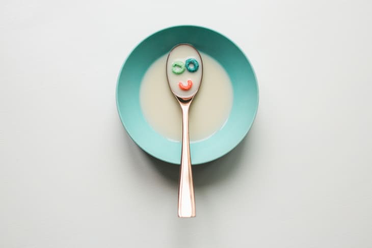 Spoon with cereal pieces forming a smiley face in a turquoise bowl of milk.