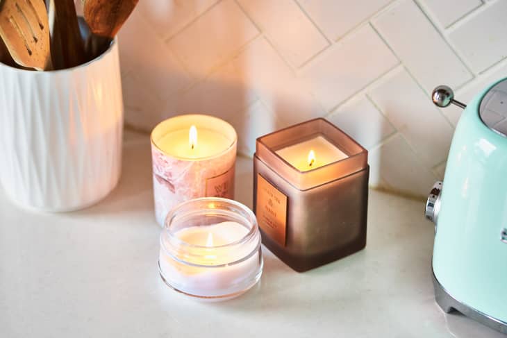 Three lit candles on a kitchen counter beside a white utensil holder and a mint green toaster.
