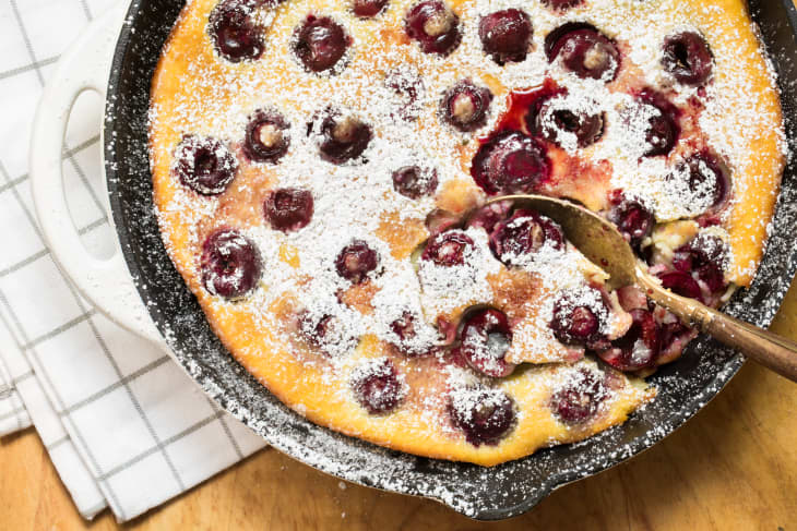 Baked clafoutis sprinkled with powdered sugar, a spoon scooping out a serving
