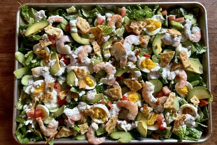sheet pan full of cut lettuce, cucumbers, celery, hard boiled jammy eggs, shrimp, avocado, chips, cheese, sauce