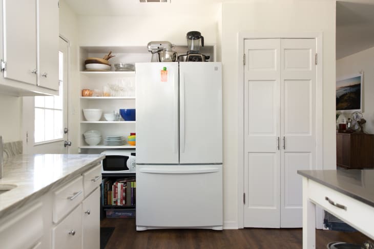 White kitchen with a double-door fridge, open shelves with dishes, and a countertop mixer.