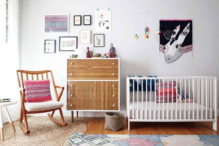 Nursery with wooden rocking chair, colorful pillows, crib, dresser, and wall art.