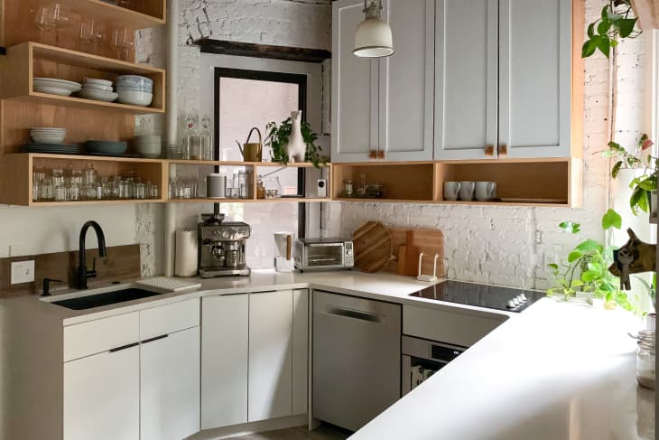 Modern kitchen with white cabinets, open wooden shelves, coffee machine, toaster, and potted plants by the window.