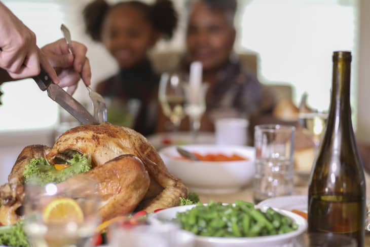 Man carves the roasted turkey on platter during Thanksgiving or Christmas dinner. Vegetables and trimmings around turkey.