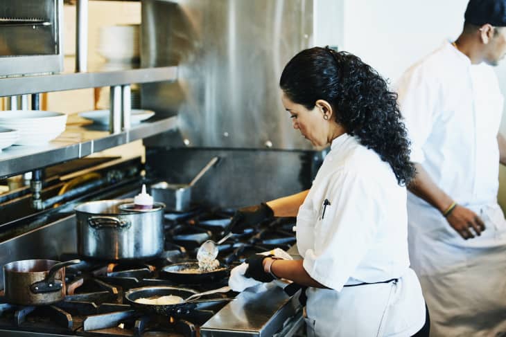 Female chef preparing food at stove in restaurant kitchen
