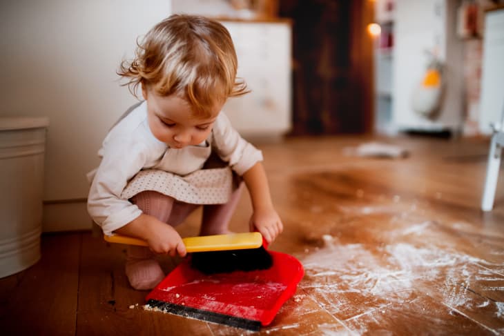 A small toddler girl with brush and dustpan sweeping floor in the kitchen at home