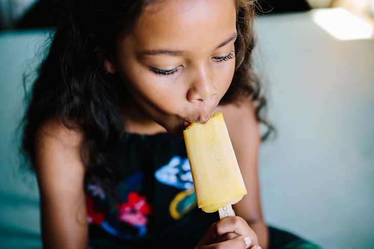 Girl eating popsicle while sitting on bed at home