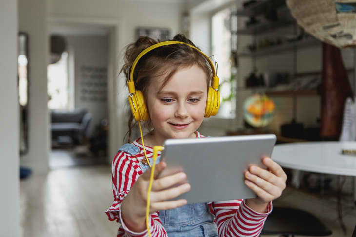 young girl at home playing with tablet or ipad wearing yellow headphones