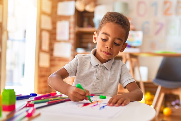 african american toddler drawing using paper and marker pen at kindergarten