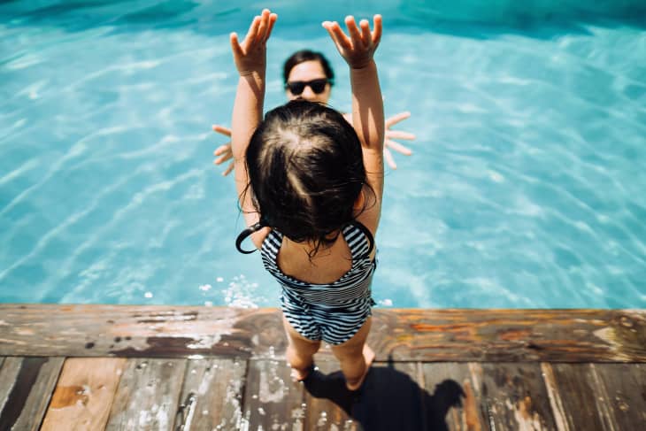Toddler having fun and jumping into her mother's arms in the swimming pool in summer.