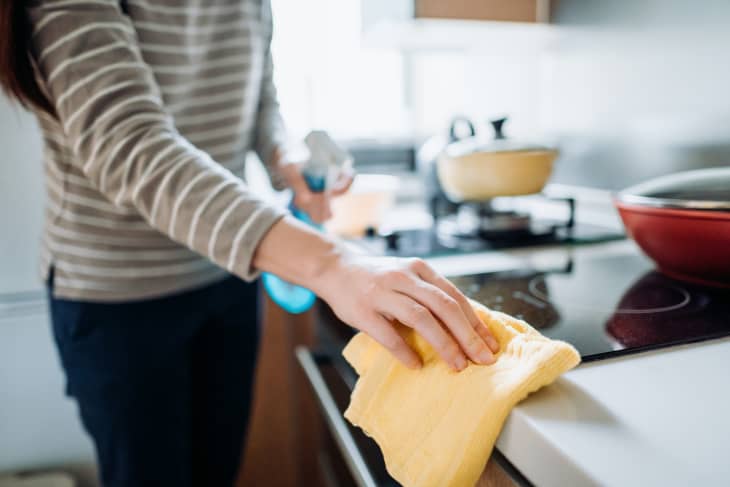 woman cleaning the kitchen counter with cleaning spray and cloth