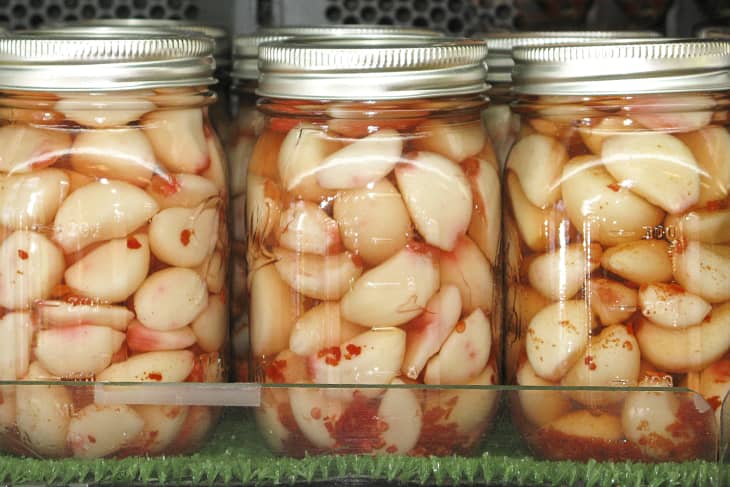 Homemade pickled garlic cloves preserved in mason jars with chopped chilli peppers - in a row.