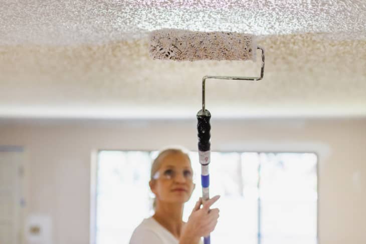 Mature Adult Female Painting Ceiling White With Paint Roller