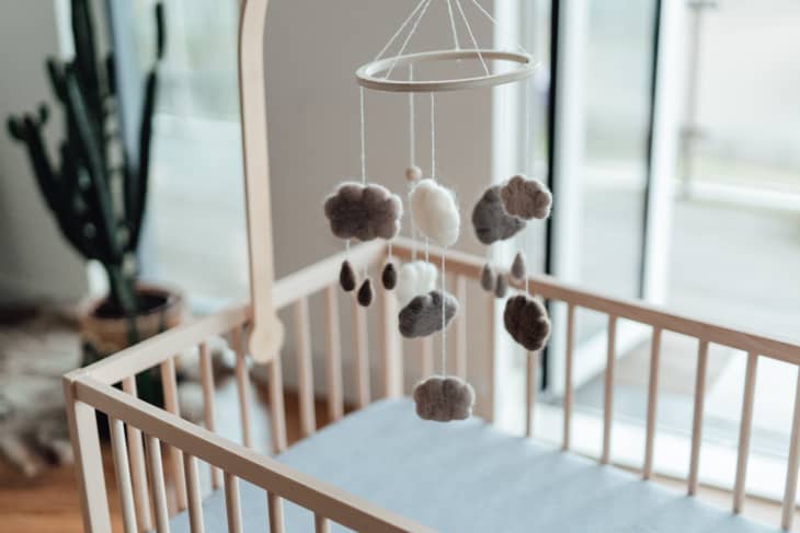 Stylish Scandinavian newborn baby nursery with natural wooden baby cot and handmade mobile hanging over it