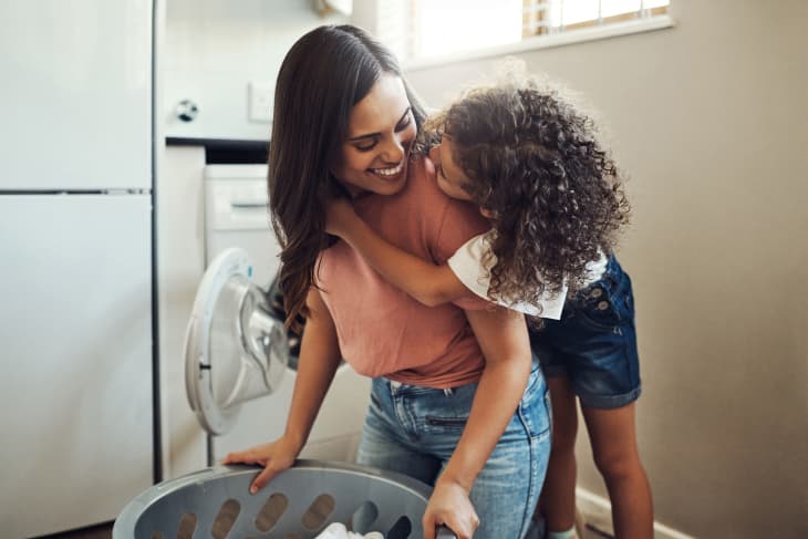 young girl hugging her mother while helping her with the laundry at home