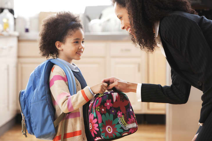 Mother in the kitchen handing her daughter a colorful lunch bag before she goes off to school