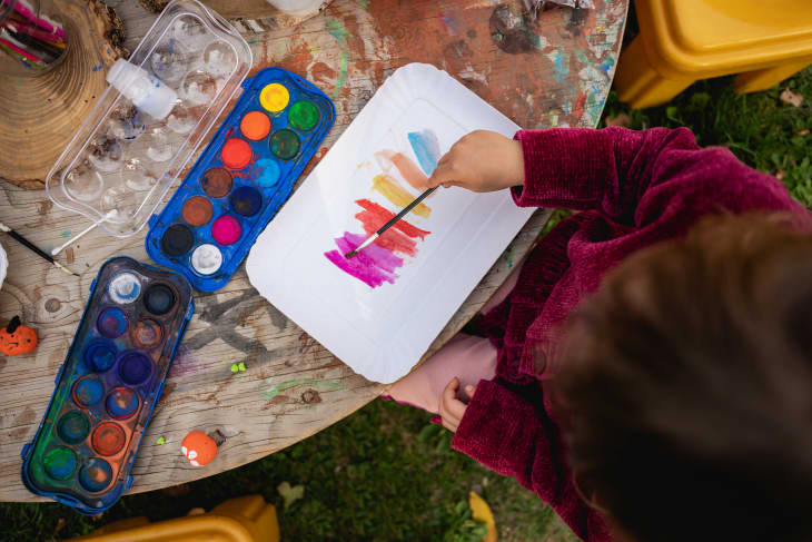 Creative activities and games for kids. Watercolor paint, overhead shot of kid painting on table outdoors, covered with paint, supplies
