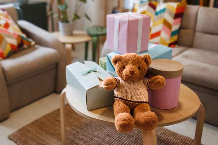 Teddy bear with gifts arranged on coffee table for baby shower party