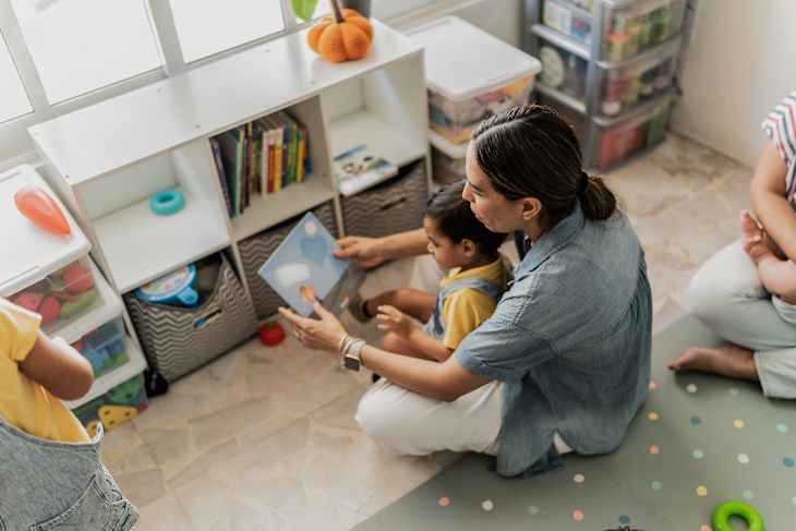 Mid adult woman reading a picture book to her son in the playroom
