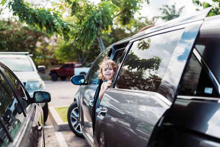 Cute little girl getting out of mini van in store parking lot