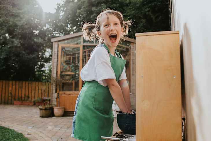 An excited little girl makes a mess in an outside 'mud kitchen'
