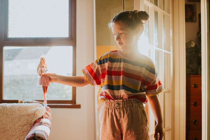 A little girl stands in a sunny room in a residential home, playing with a doll figure
